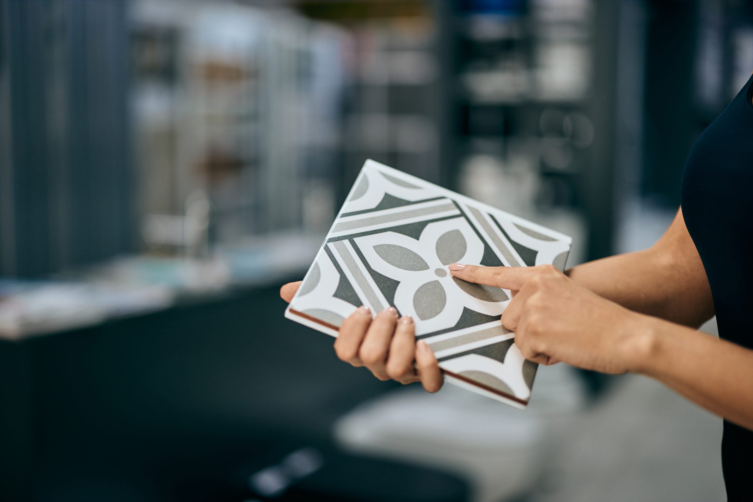 A female seller holding a ceramic tile, showing a design on it, working at the home design shop.